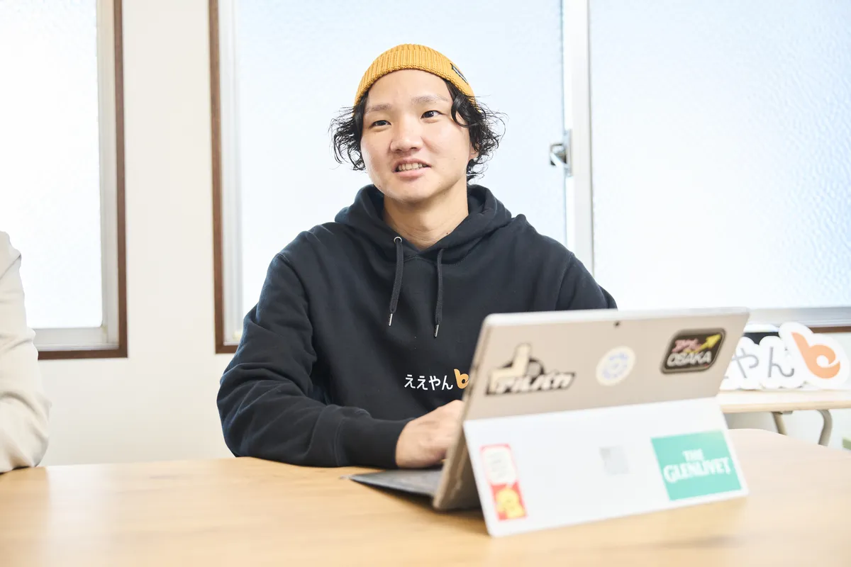 ノートパソコンを前に、打ち合わせで話すスタッフ